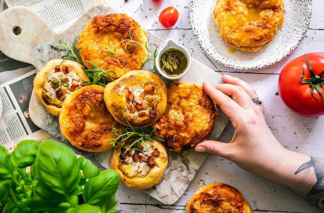 Mini tarty z boczkiem i serem, podane z oliwą z oliwek i ziołami. Zdrowe tłuszcze produkty na talerzu.