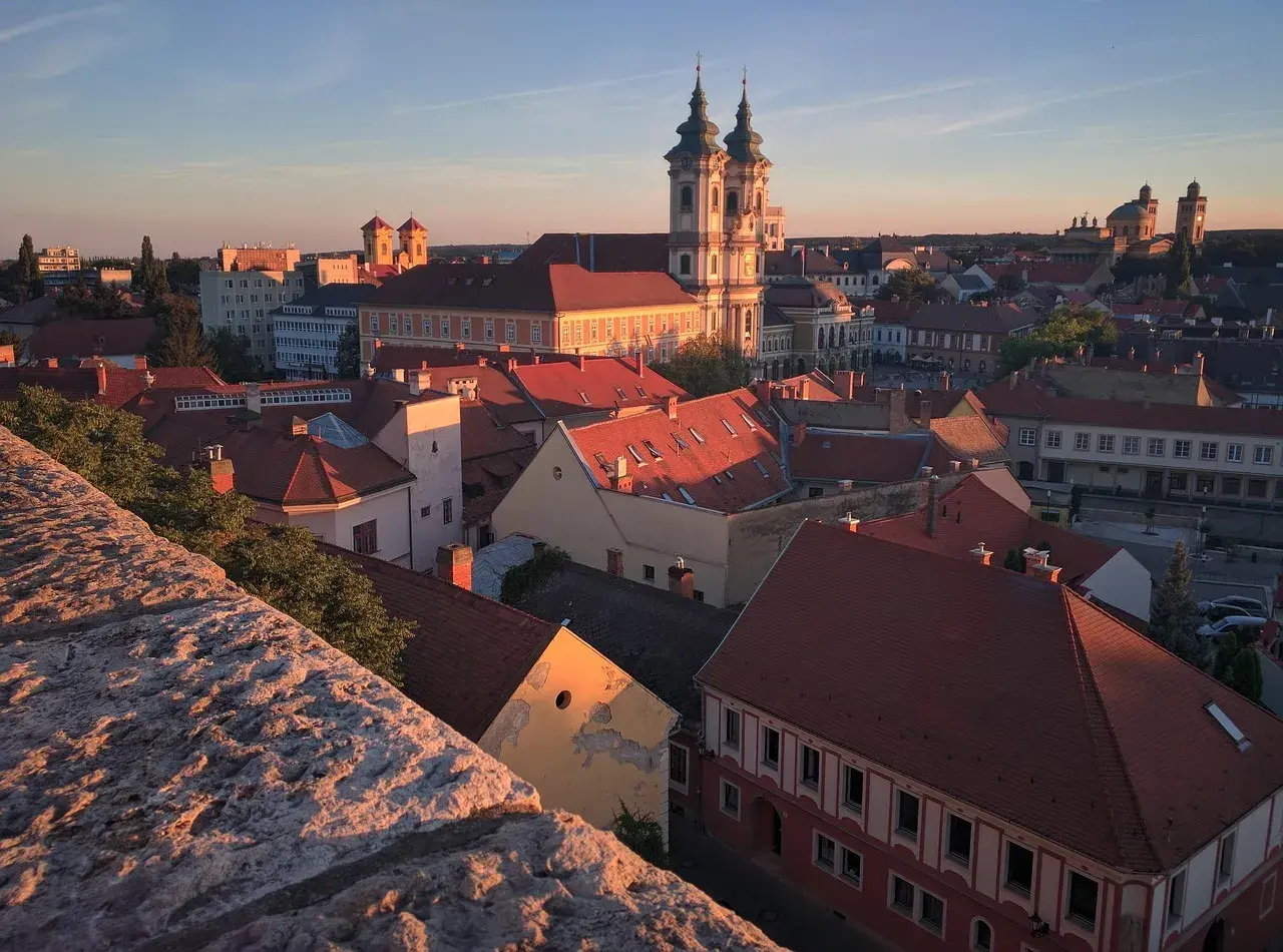 Widok na Eger z zamku o zachodzie słońca. Czerwone dachy, barokowa bazylika i wieże kościelne w złotym blasku.