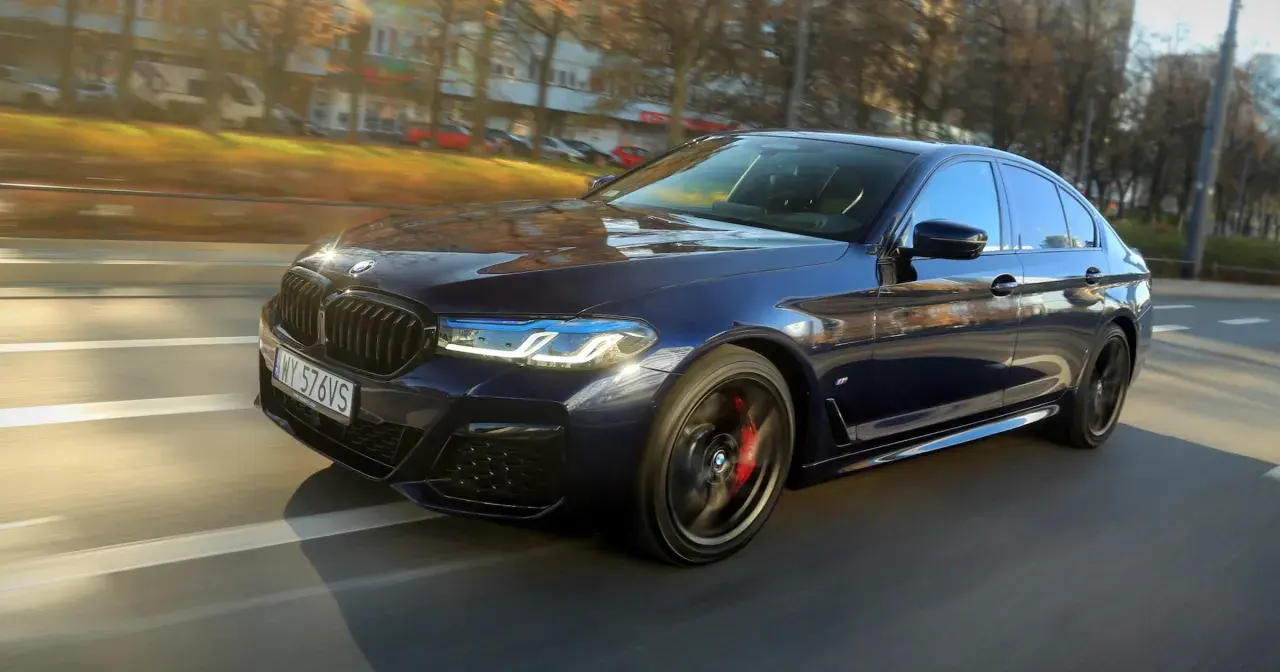 Ciemnoniebieskie BMW 540d sunie po drodze, odbijając jesienne słońce.