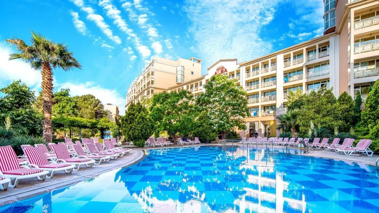 Basen z leżakami i palmą przy hotelu Alba w Bułgarii. Słoneczny dzień, błękitne niebo z chmurami.