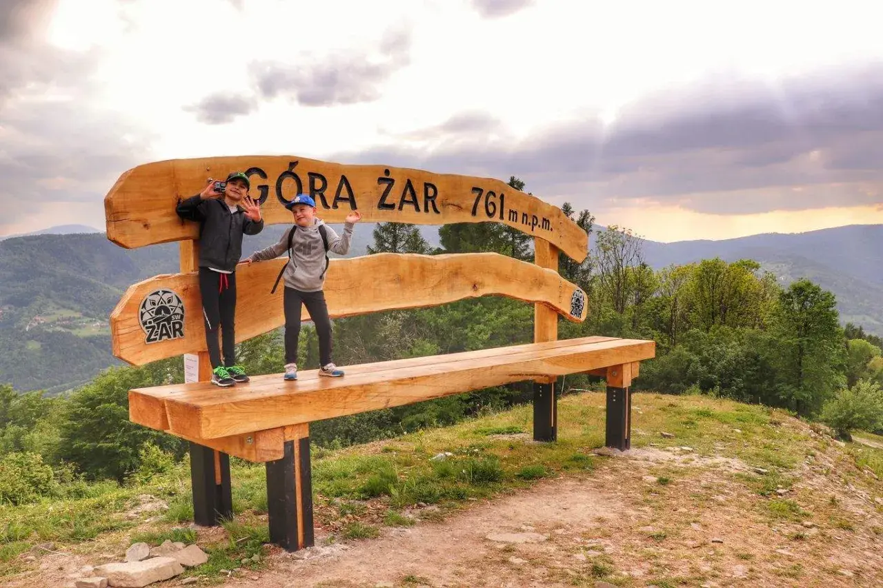 Dzieci pozują na ławce na szczycie Góry Żar (761 m n.p.m.), ciesząc się widokiem i trasą.