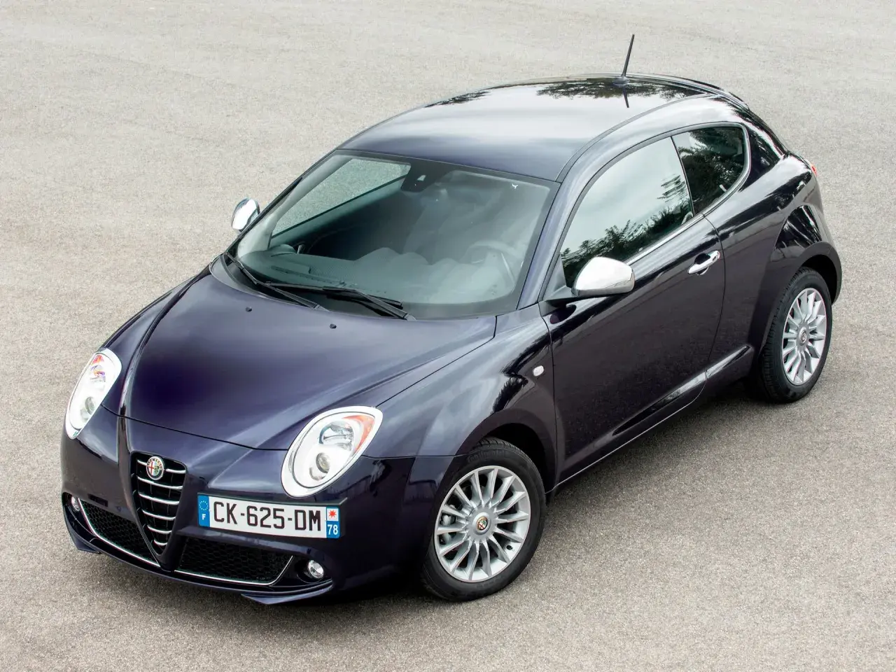 Elegancki, granatowy Alfa Romeo MiTo na tle asfaltu. Wiele osób szuka alfa romeo mito opinie, by poznać ten model.