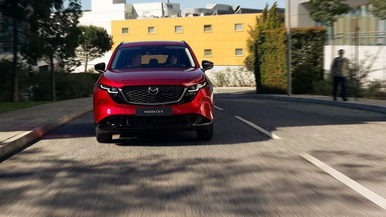 Czerwona Mazda CX-5 jedzie ulicą. W tle budynki i drzewa.