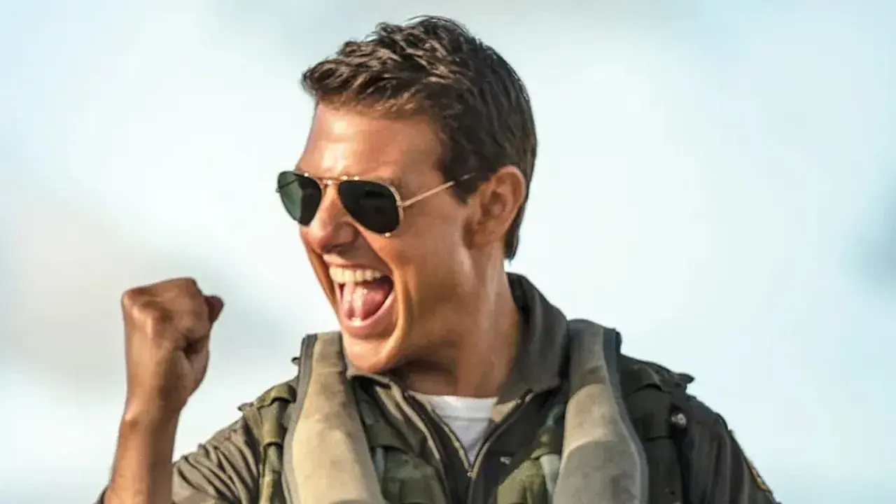 Tom Cruise w okularach przeciwsłonecznych i kurtce pilota, z zaciśniętą pięścią, krzyczy z radości. Czekamy na **Top Gun 3**!