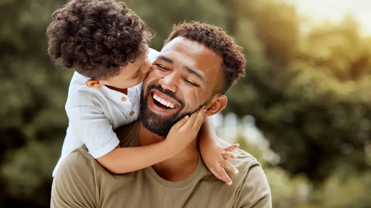 Un niño abraza a su padre, quien ríe feliz. Un momento tierno que inspira frases de padres a hijos para reflexionar sobre el amor.