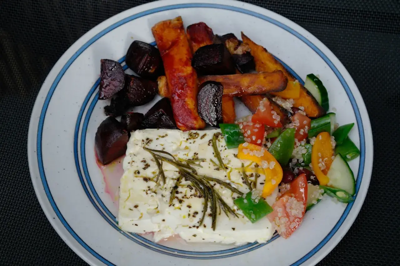En tallrik med ugnsbakade rödbetor, sötpotatisstavar och en stor bit fetaost i ugn, toppad med örter. Serveras med en fräsch sallad.