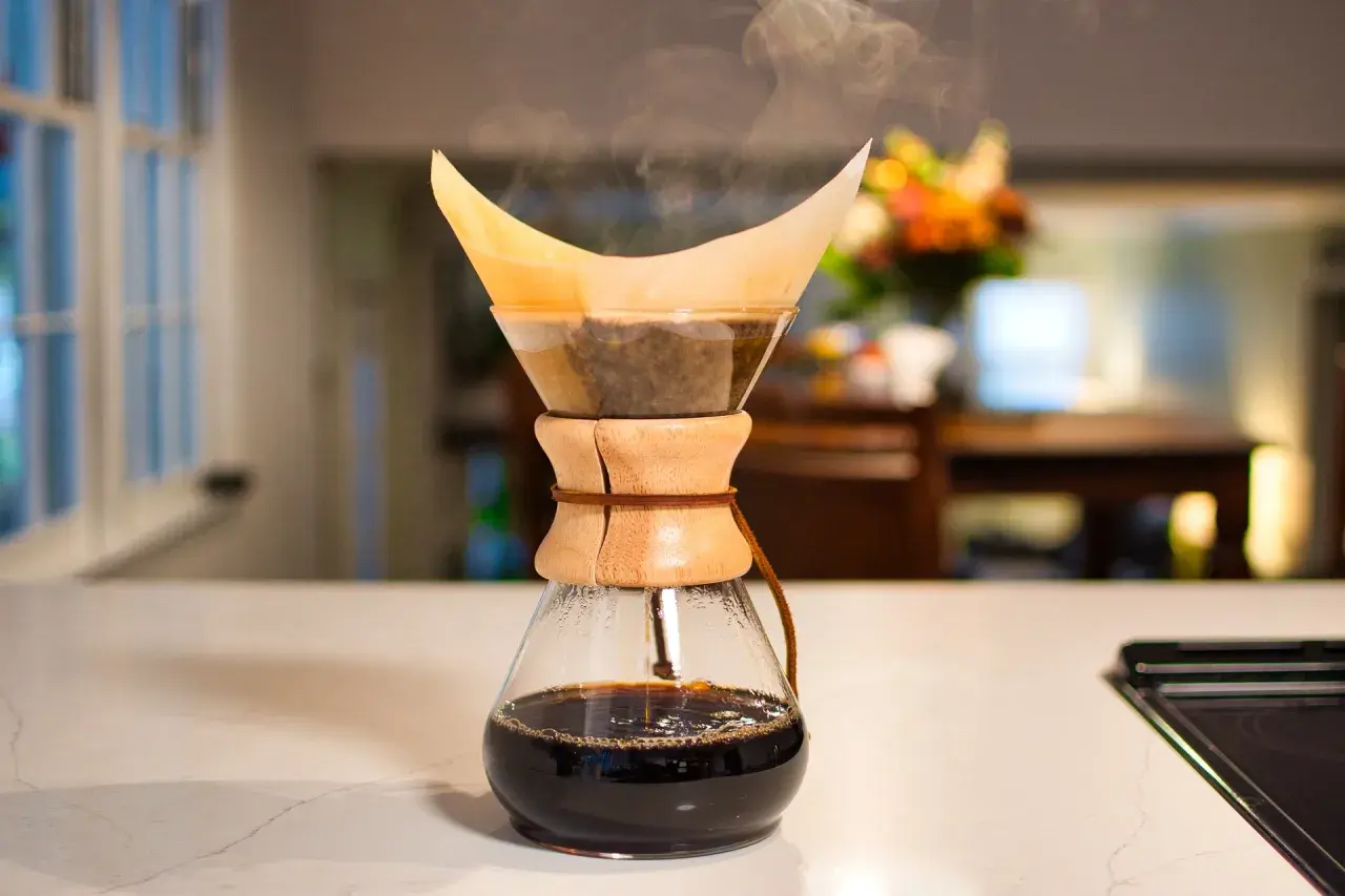Dampf steigt auf bei der Chemex Zubereitung. Frisch gebrühter Kaffee tropft in die Glaskaraffe.