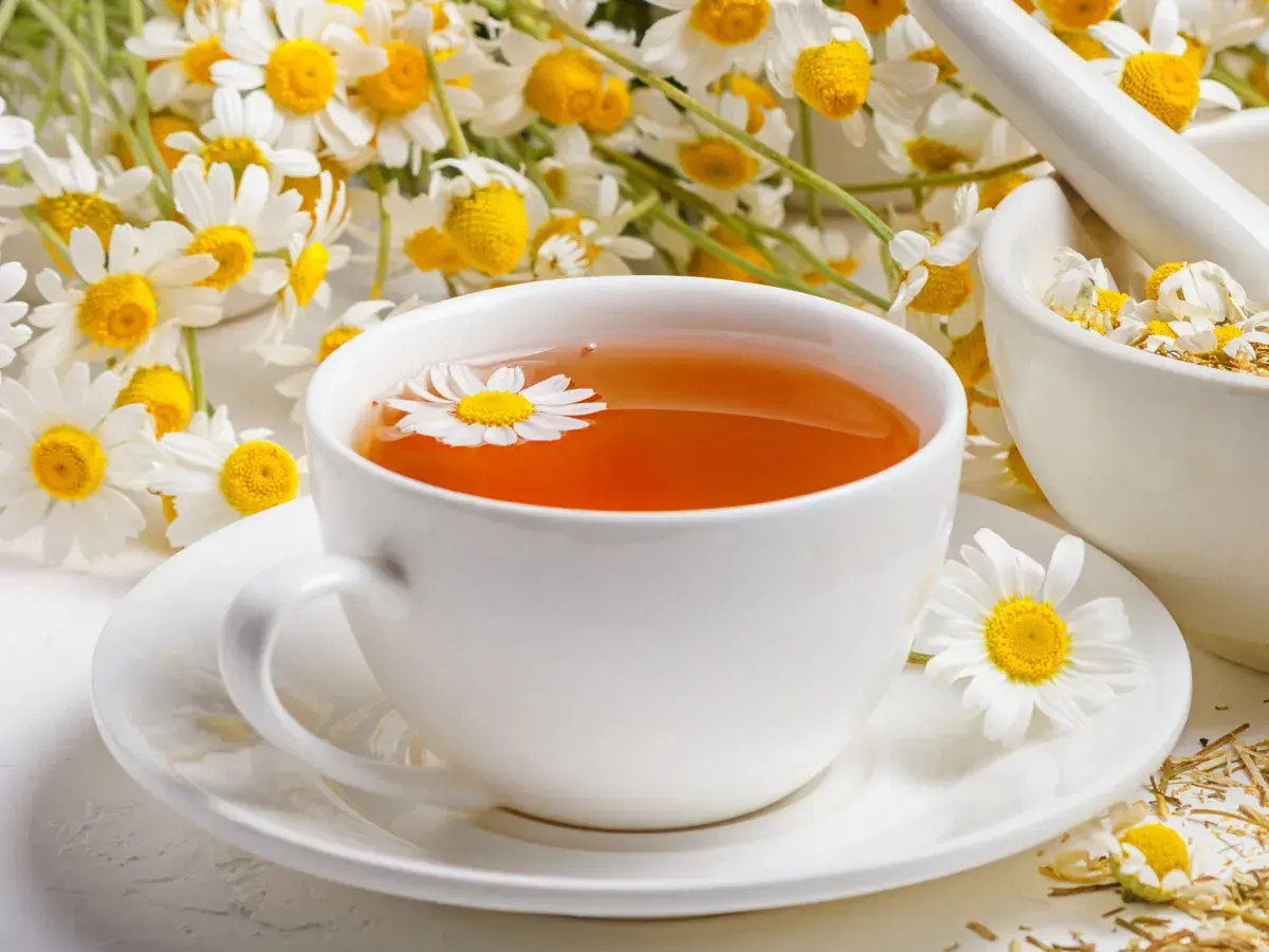 Aromatyczne picie rumianku w filiżance, obok świeżych kwiatów i moździerza z suszem.