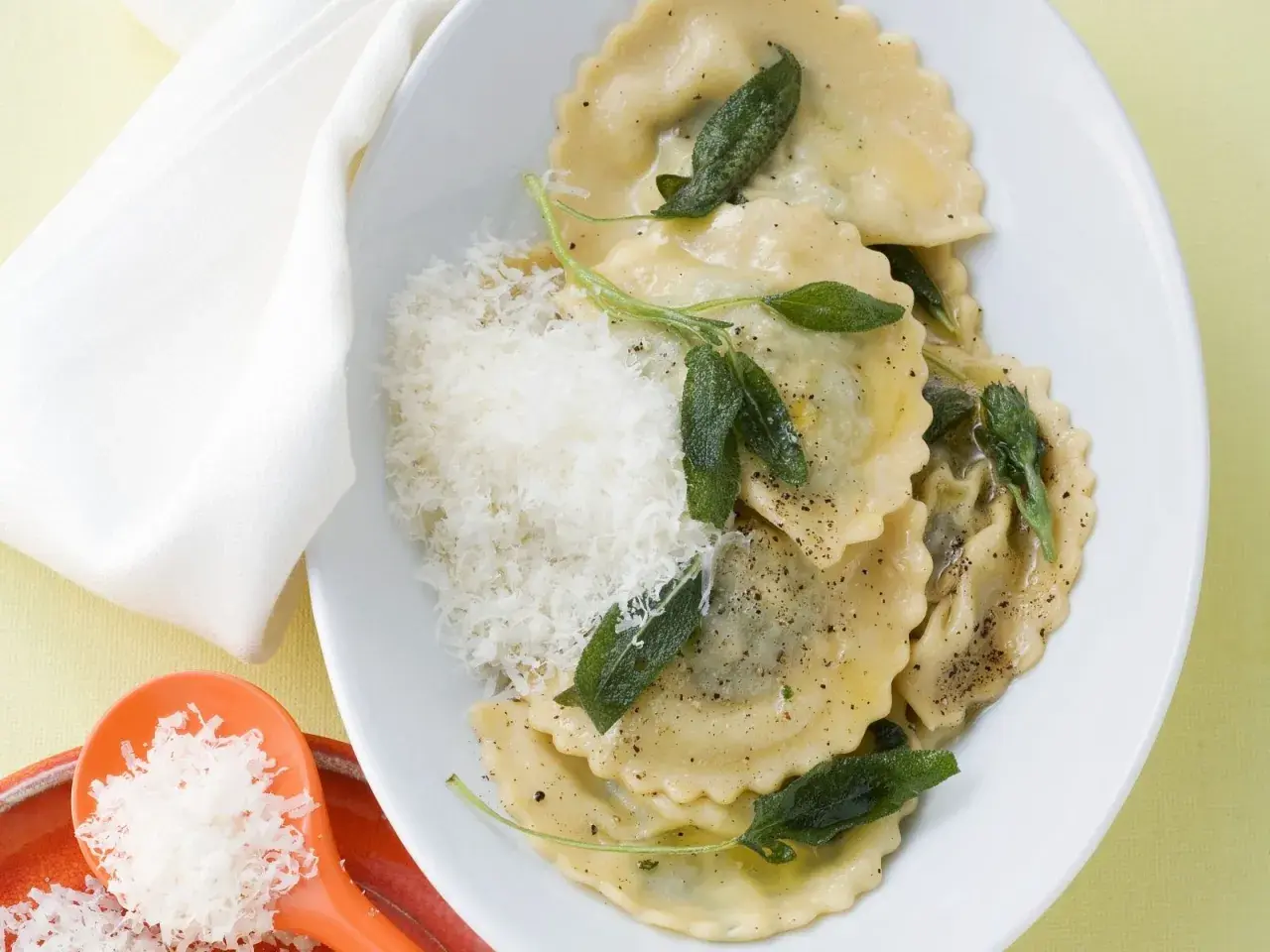 Ravioli mit Spinat-Ricotta-Füllung, Salbeiblättern und geriebenem Parmesan auf einem Teller.