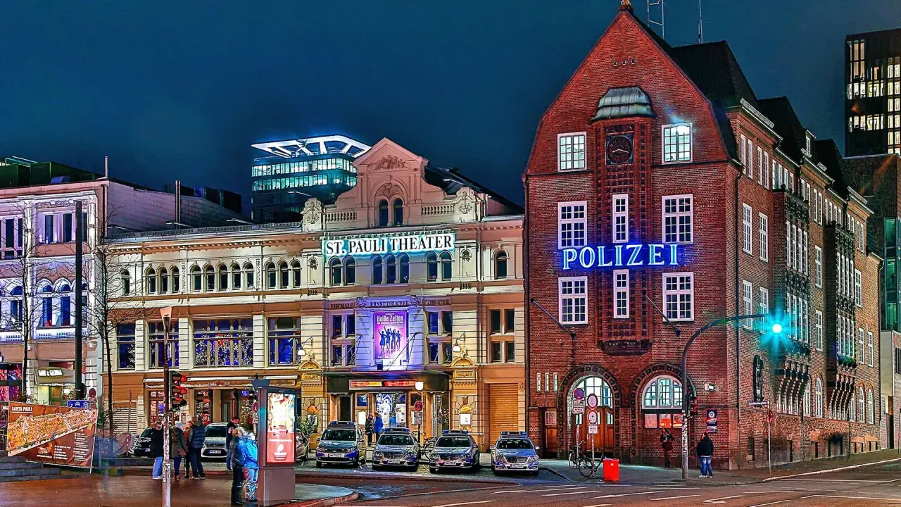 Polizeigebäude und St. Pauli Theater in Hamburg bei Nacht, mit leuchtenden Schildern und Autos.