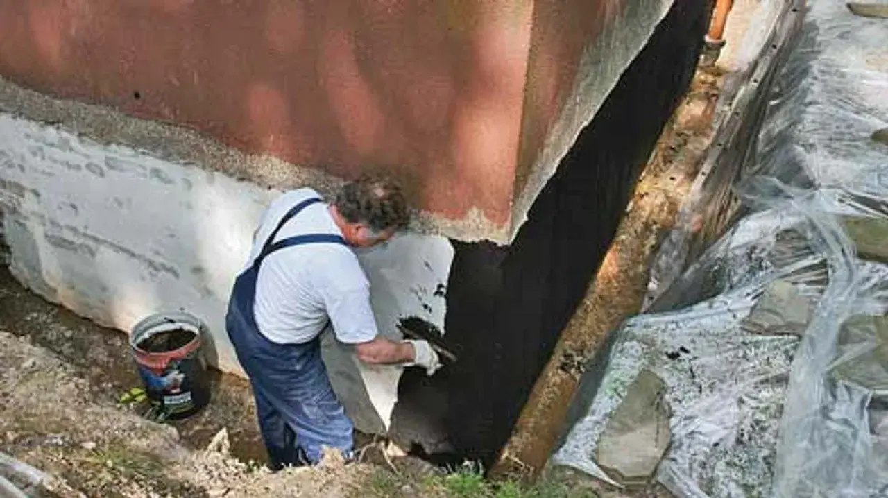 Mann trägt Bitumenanstrich innen auf die Kellerwand auf.