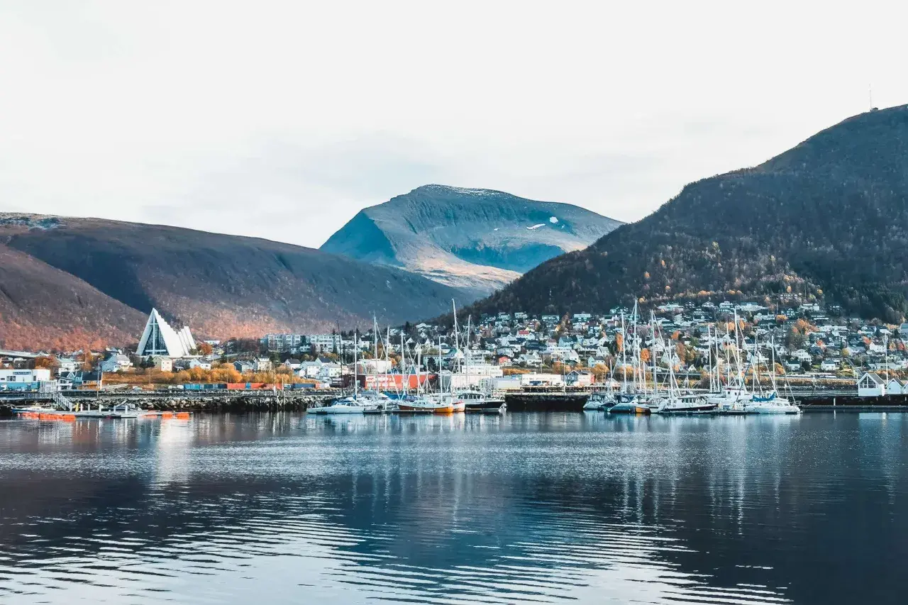 Tromsø im Sommer: Segelboote im Hafen vor einer Stadt am Berghang, gekrönt von der markanten Eismeerkathedrale.