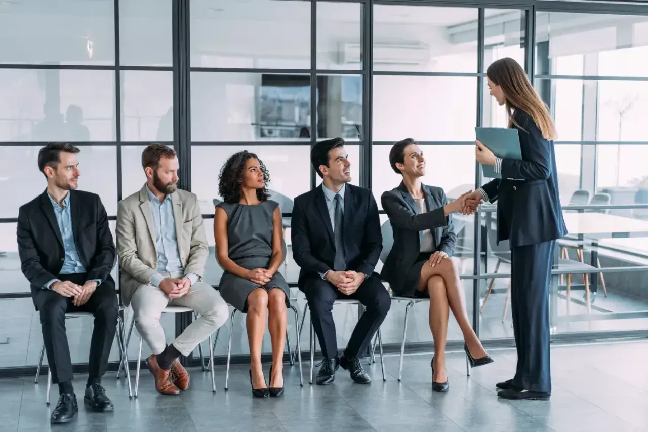Candidatos esperan su turno para una entrevista de trabajo. Una mujer saluda a otra, un paso clave en la adaptacion laboral.