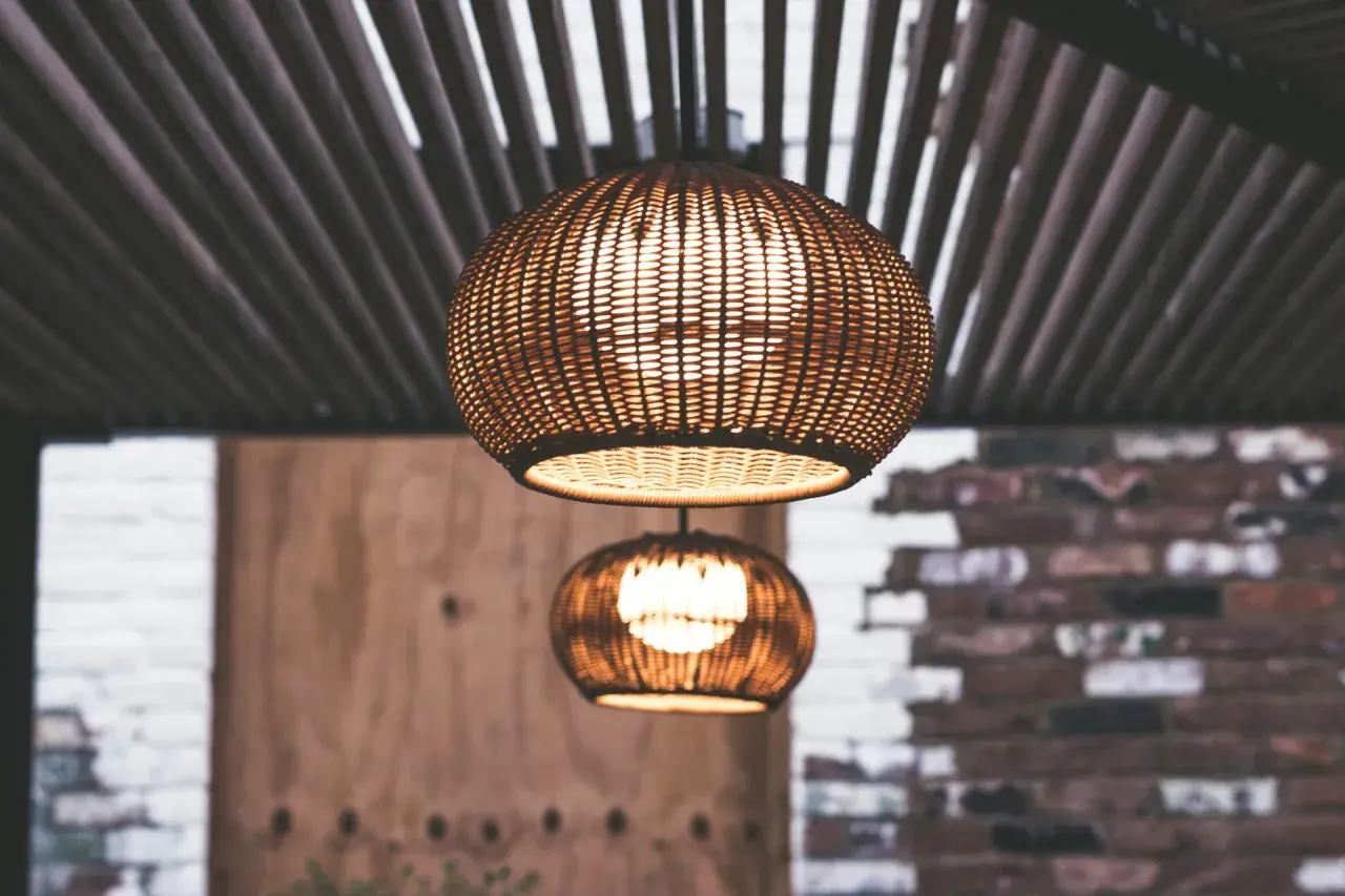 Dos lámparas de mimbre esféricas cuelgan bajo un techo de listones. La luz cálida que emiten crea un ambiente acogedor, con unos agradables lúmenes por m2.