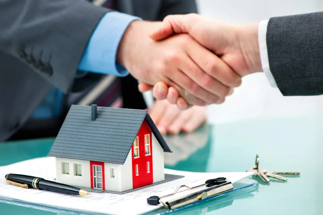 Accordo per un contratto di locazione: stretta di mano su un modello di casa, penna e chiavi.