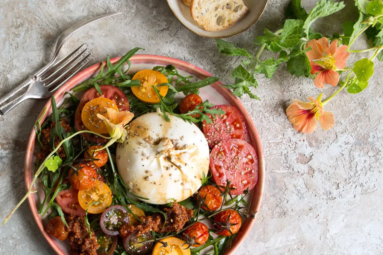 Ein bunter Tomaten Burrata Salat mit Rucola und essbaren Blüten.