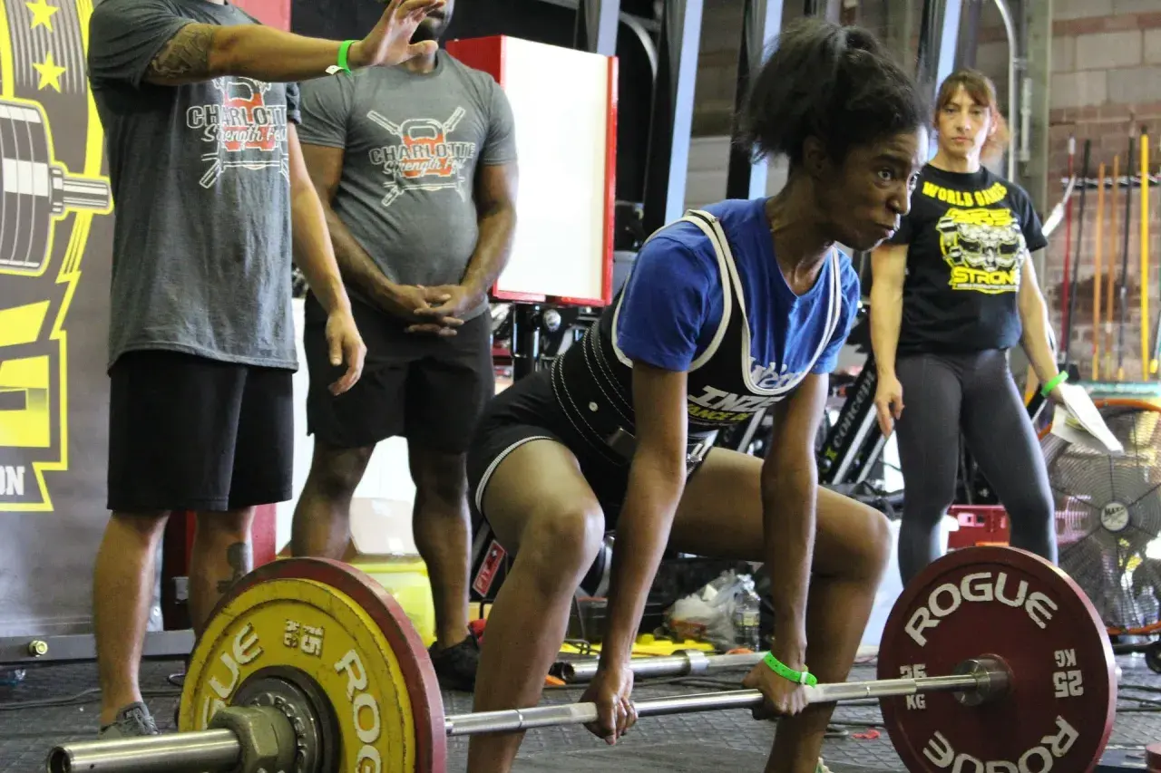 Atleta si prepara per uno stacco da terra, concentrata. Un evento di powerlifting e weightlifting con pubblico e attrezzature.