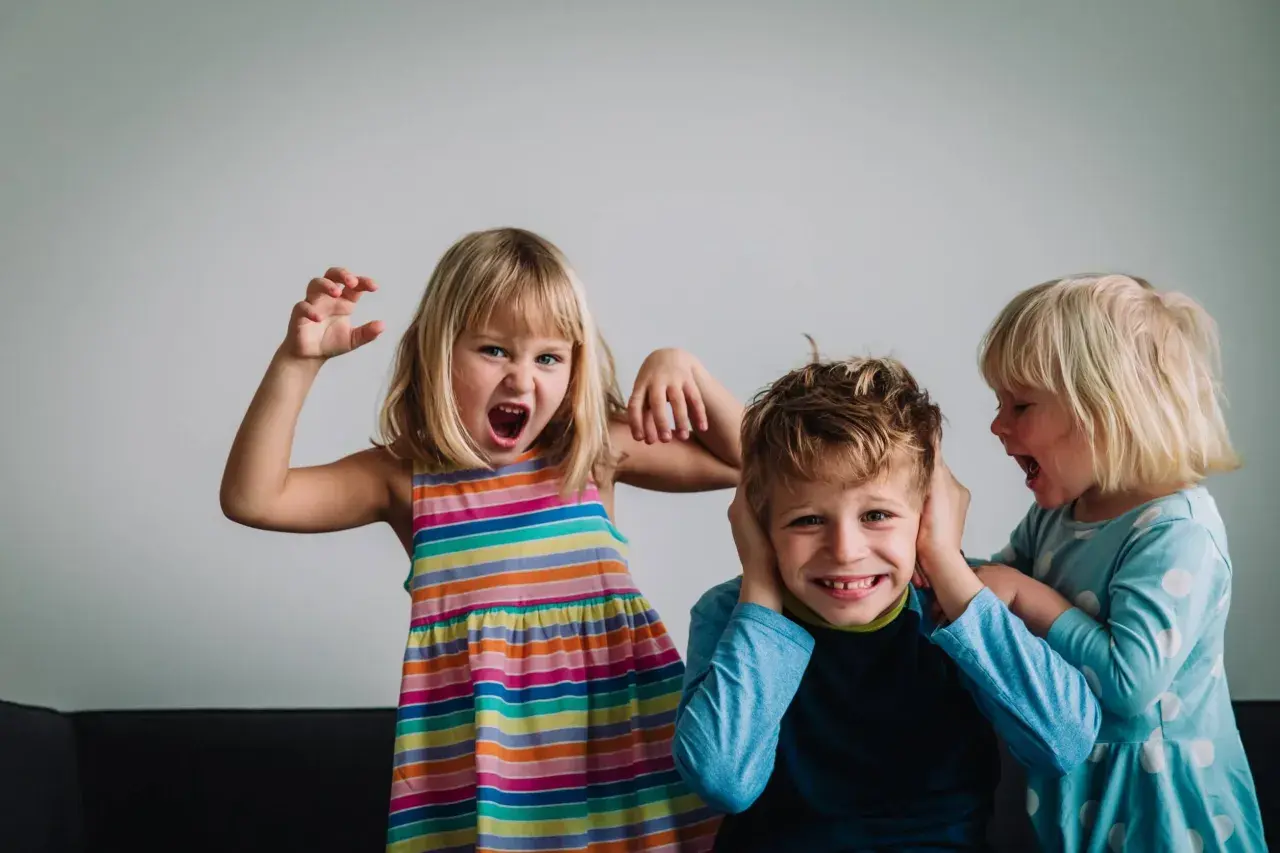 Niños expresando emociones fuertes. Una niña grita y hace gestos, otra le tapa los oídos a un niño que se ríe. Un ejemplo de la complejidad de la inteligencia emocional niños.