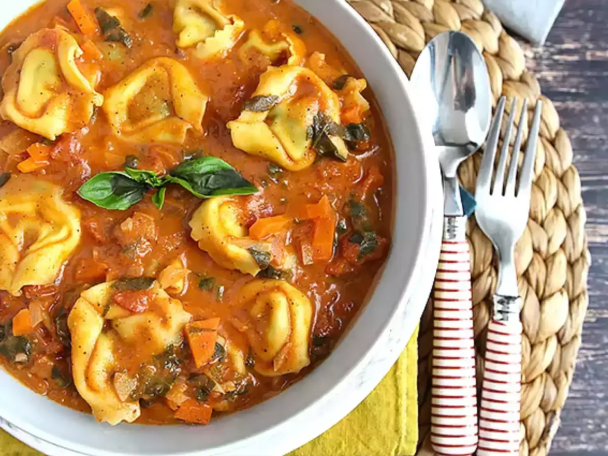 Miseczka tortellini w sosie pomidorowym z bazylią, obok sztućców.