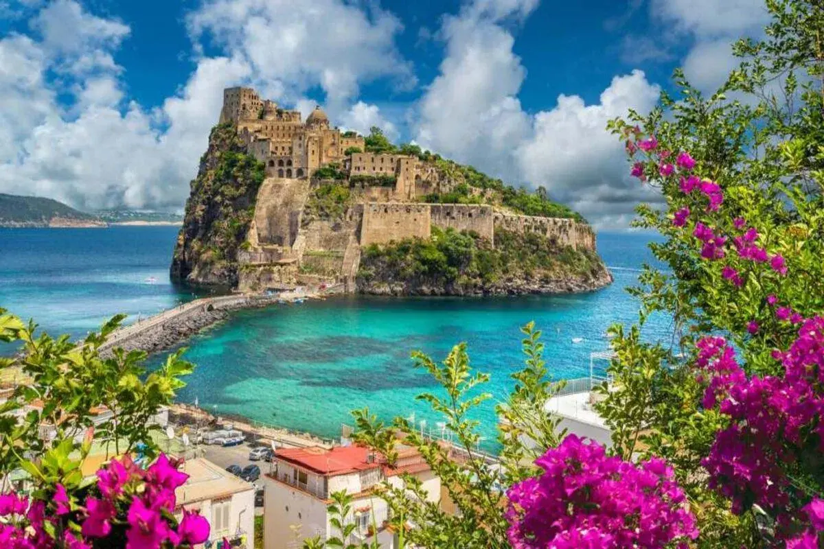 Castello Aragonese su uno scoglio, con mare turchese e fiori viola in primo piano. Una vittoria colonna di bellezza naturale.