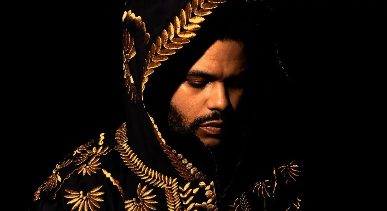 The Weeknd w czarnej, haftowanej złotem bluzie z kapturem, zamyślony. Jego utwory często opowiadają o mrocznych stronach życia.