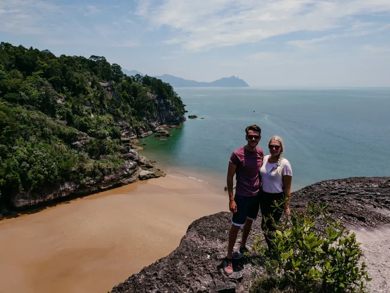 Ein Paar genießt die Aussicht auf eine tropische Bucht mit Sandstrand und Dschungel. Tolle Malaysia Urlaub Erfahrungen!