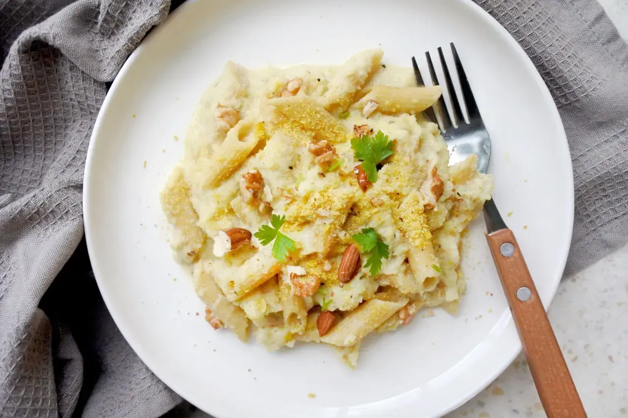 Penne z kremowym sosem z kalafiora, orzechami i natką pietruszki. Pyszny makaron z kalafiorem na białym talerzu.