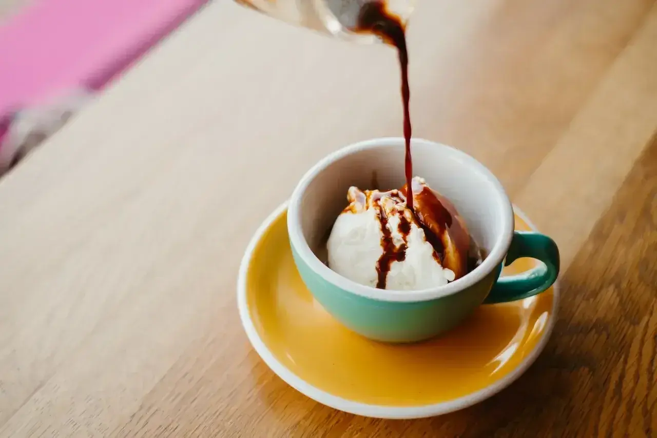 Gorące espresso zalewa kulkę lodów waniliowych w filiżance. Klasyczne lody po włosku, idealne na deser.