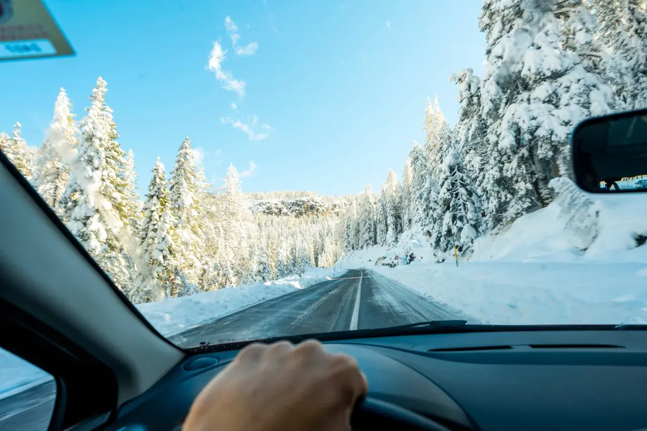Conduciendo por una carretera nevada, rodeada de árboles cubiertos de blanco. Consejos para como conducir con nieve.