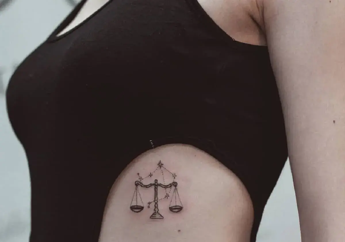 Delikatny tatuaż waga znak zodiaku na boku, ozdobiony gwiazdami.