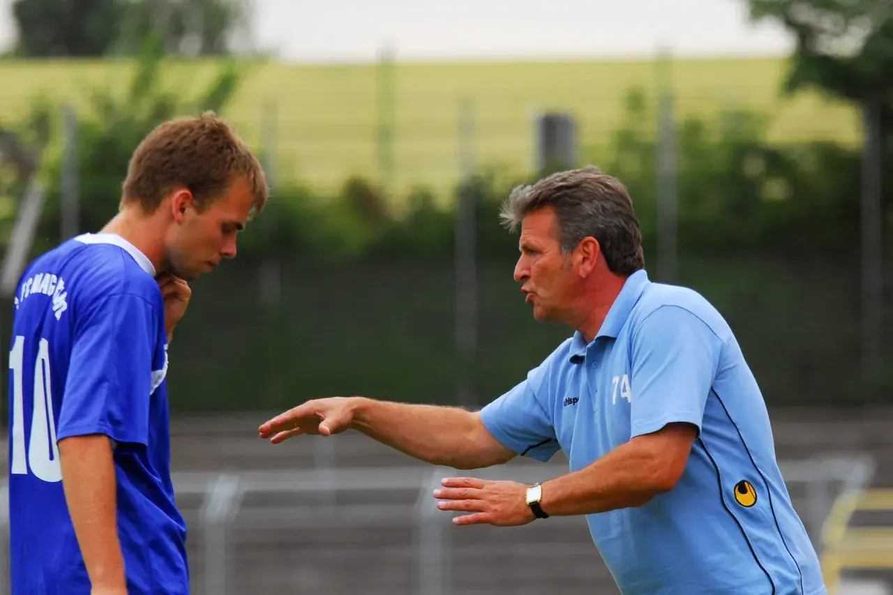 Trainer Martin Hoffmann gibt einem Spieler Anweisungen auf dem Fußballplatz.