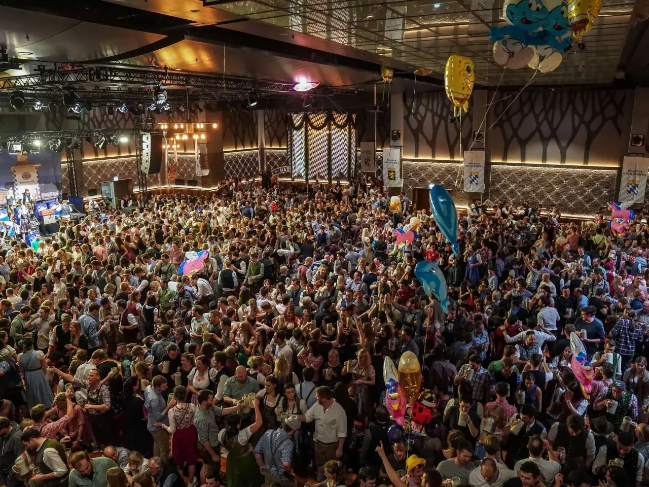 Volles Festzelt am Nockherberg 2026 mit vielen Menschen in Tracht, die Bierkrüge schwenken. Luftballons steigen auf.