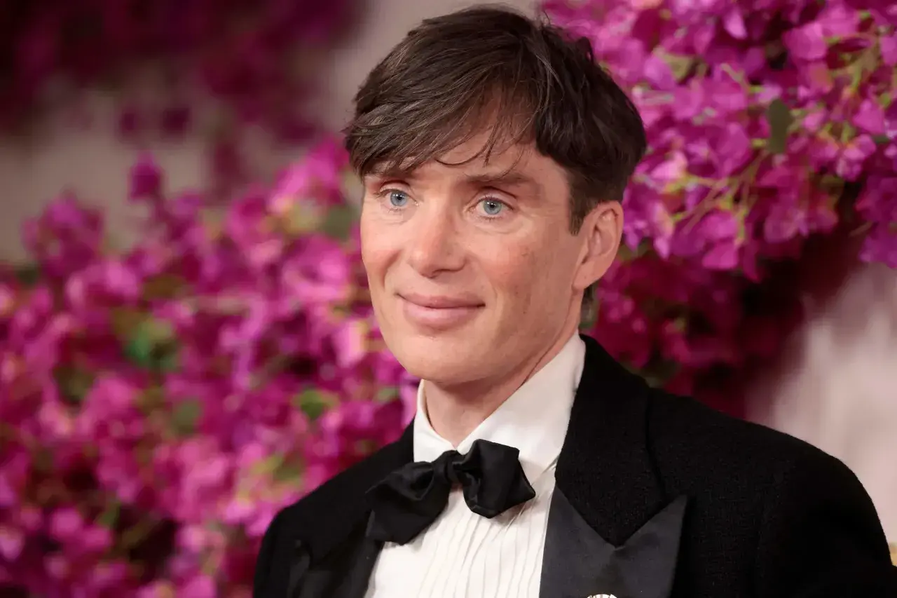 Cillian Murphy, l'attore di Oppenheimer, con un sorriso enigmatico e occhi azzurri penetranti, indossa un elegante smoking con papillon nero.