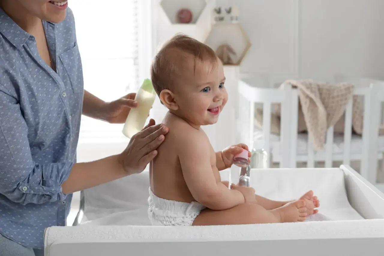Mama delikatnie wmasowuje w plecy dziecka olejek migdałowy do kąpieli. Uśmiechnięty maluch trzyma buteleczkę z płynem.