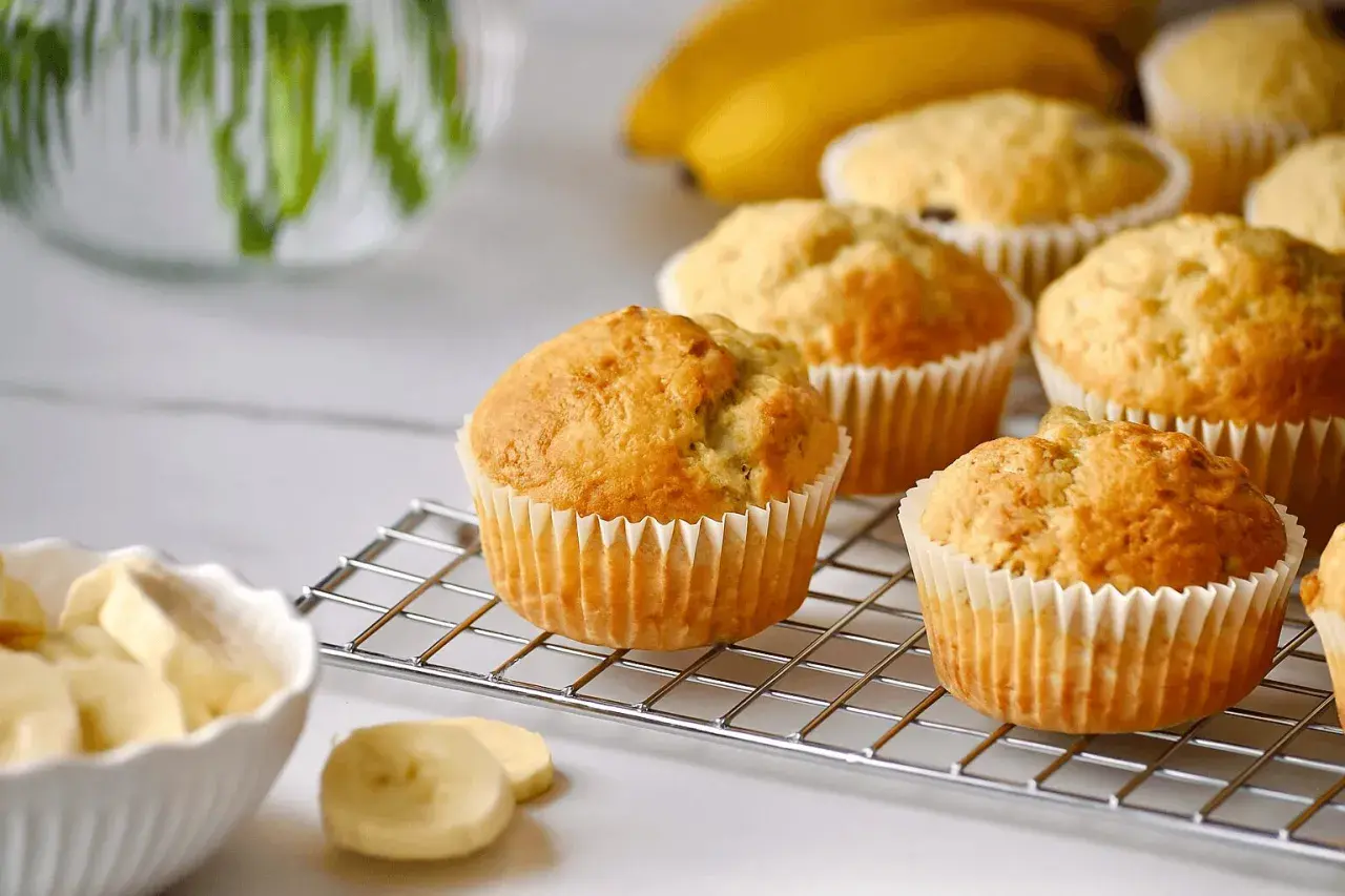 Frisch gebackene bananen muffins auf einem Kuchengitter, daneben eine Schüssel mit Bananenstücken.
