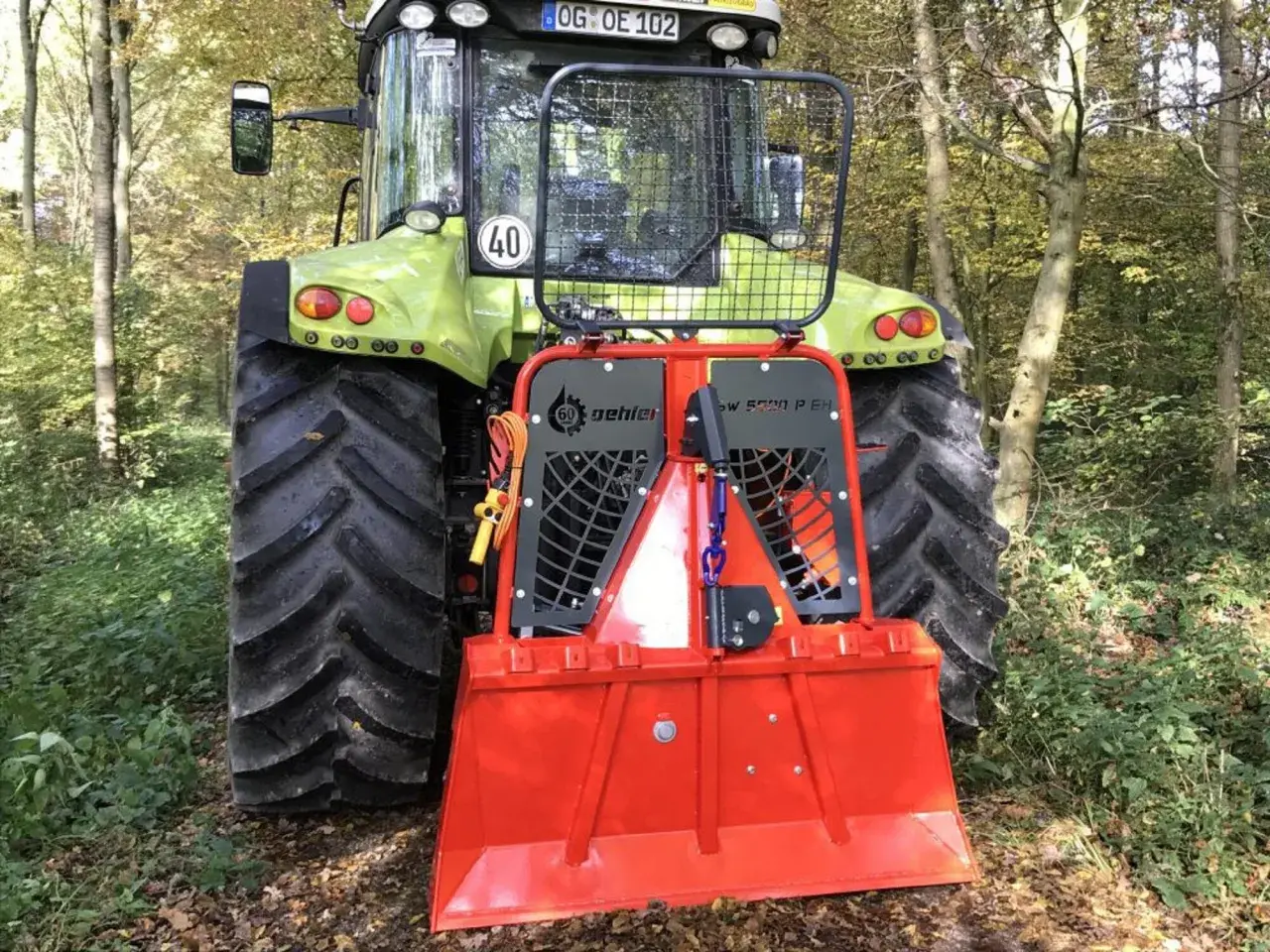 Ein grüner Traktor mit einer roten Forstseilwinde im Wald. Die Seilwinde ist bereit für den Einsatz, um Holz zu ziehen.