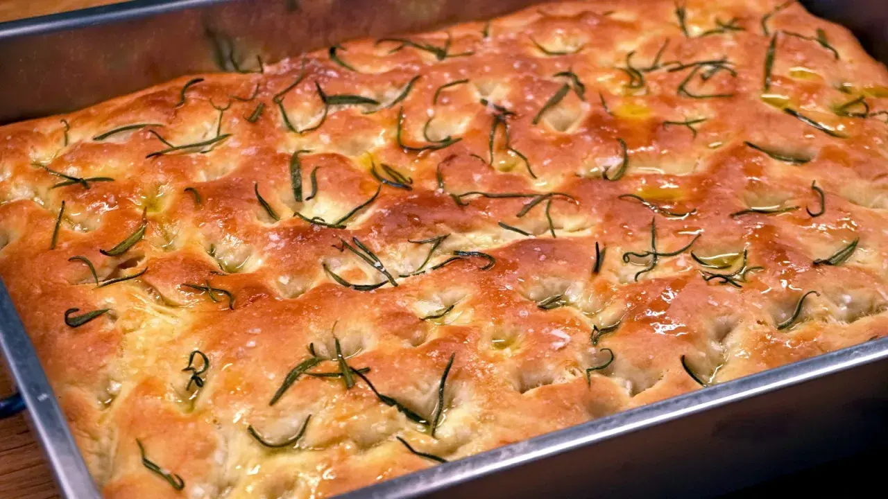 En gyllene focaccia barese med rosmarin och flingsalt i en form. Doftar ljuvligt!