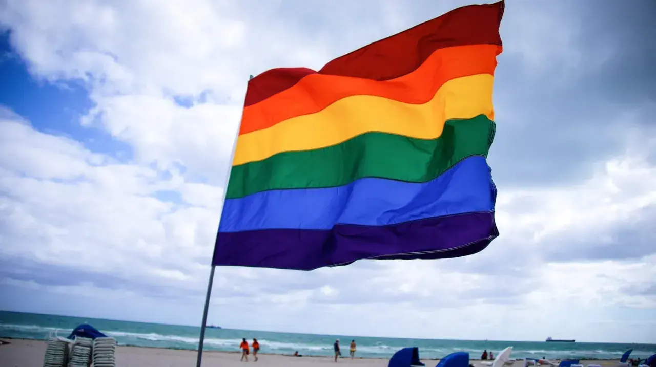 Tęczowa flaga na plaży, symbol akceptacji i wolności, w opozycji do szkodliwej terapii konwersyjnej w Polsce.