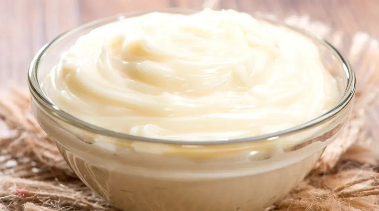 Gładki, kremowy majonez bez jajek w szklanej miseczce, ułożonej na rustykalnym tle.