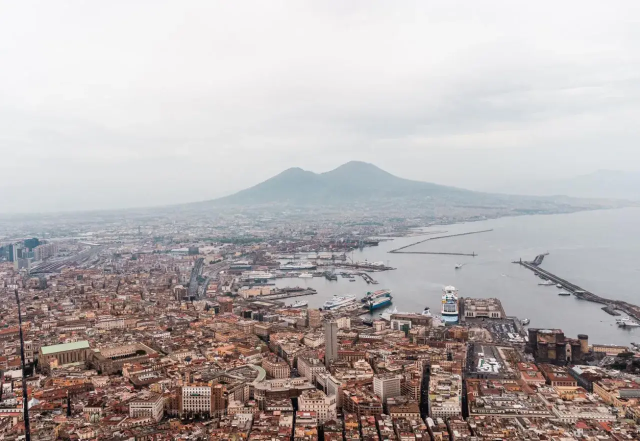 Panoramic view of Napoli, Naples, with Mount Vesuvius looming in the distance over the bustling port and city.