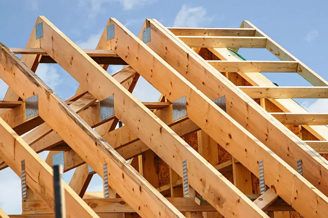 Structure en bois d'une charpente simple, avec des poutres assemblées par des équerres métalliques sous un ciel bleu.