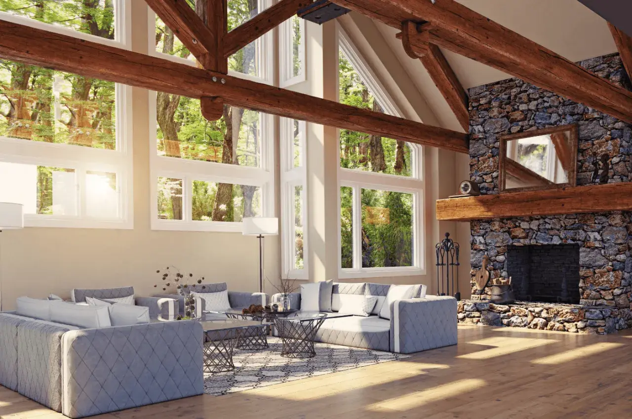 Vaste salon avec cheminée en pierre et un impressionnant plafond cathédrale bois. De grandes fenêtres donnent sur une forêt luxuriante.