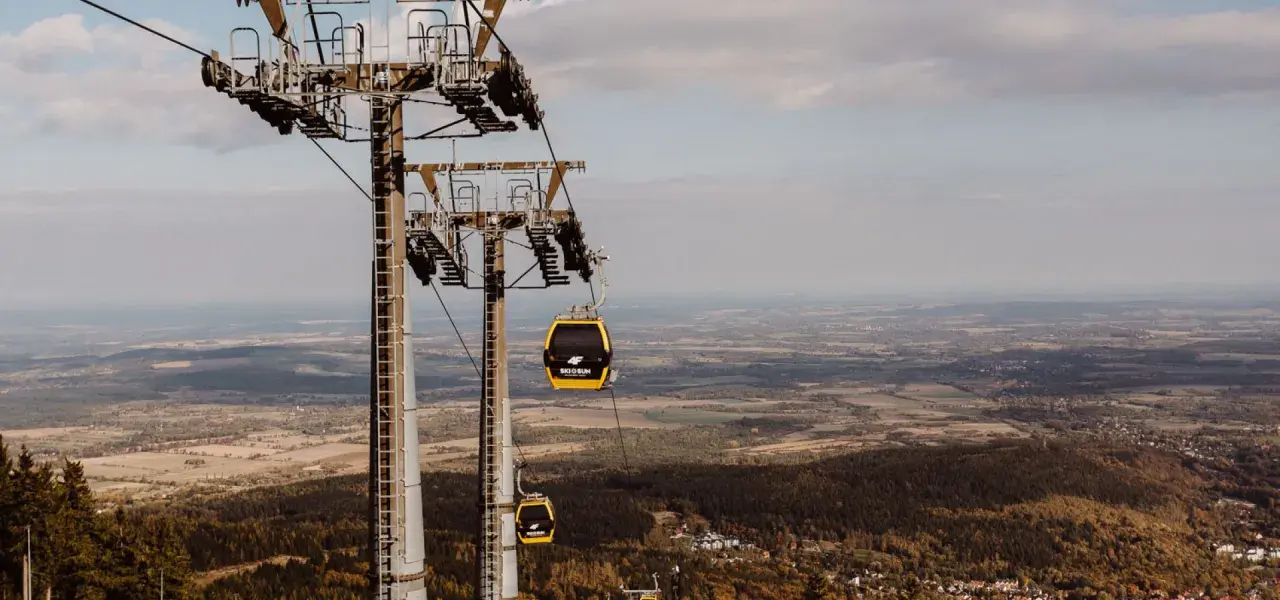 Kolejka linowa, niczym żółty roller coaster, wznosi się nad jesiennym krajobrazem.