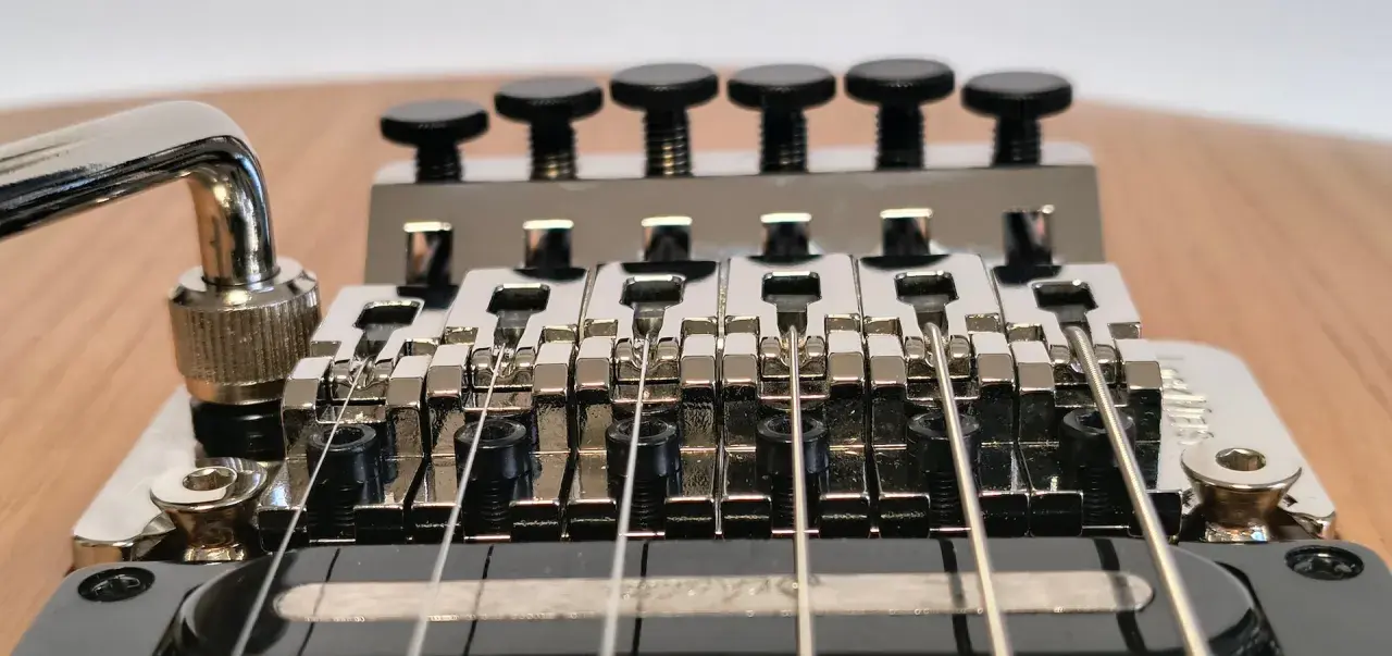 Gros plan sur le chevalet d'une guitare électrique, avec le bras de trémolo visible. Les six pontets chromés sont alignés, prêts à produire des notes vibrantes grâce au système de tremolo.