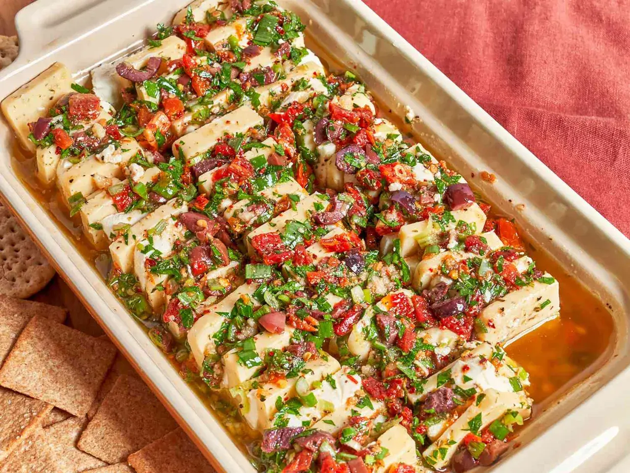 Un plat de fromage blanc coupé en tranches, garni d'olives, de tomates séchées et d'herbes. Une excellente idée repas pour l'apéritif.