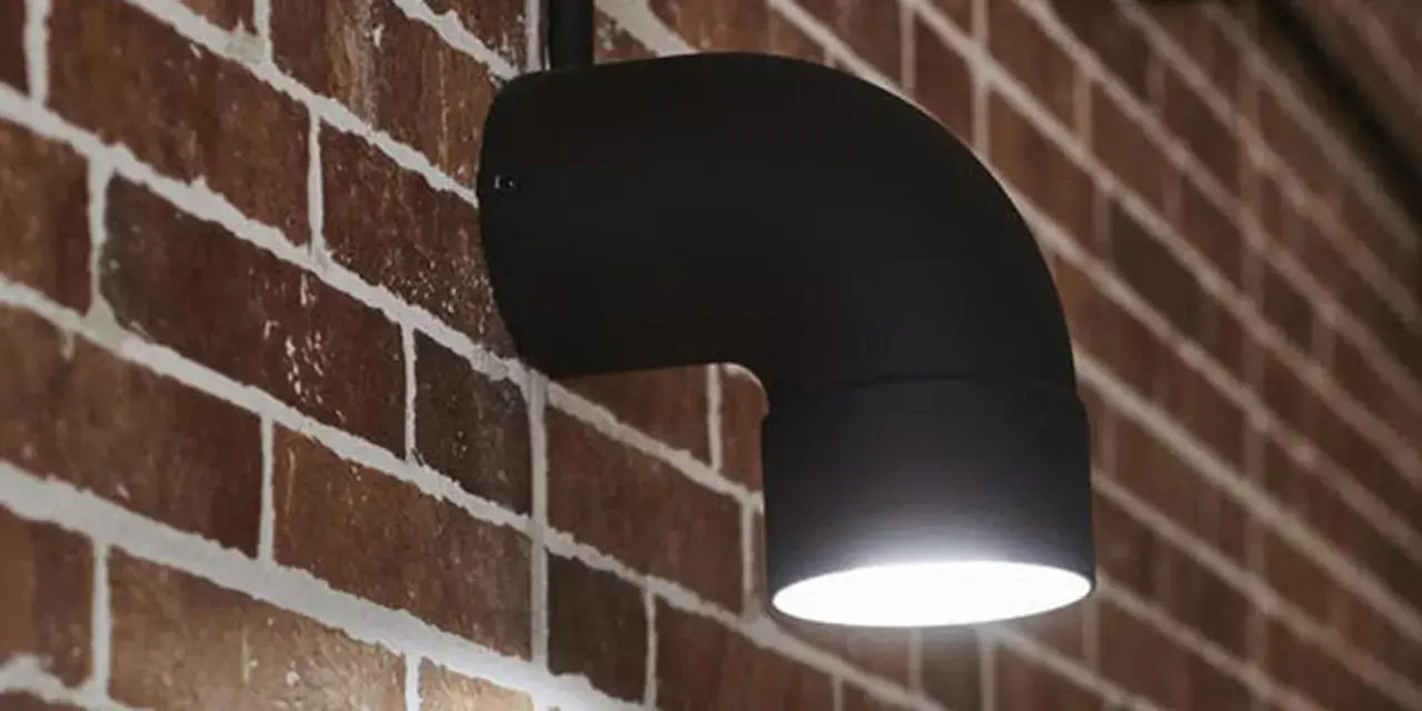 Applique fai da te in metallo nero a forma di gomito, illumina una parete in mattoni rossi.