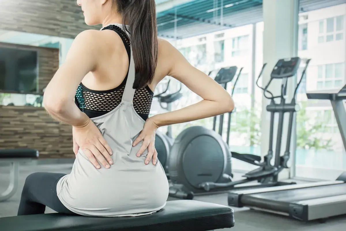 Donna in palestra con le mani sulla schiena, soffre di mal di schiena. Attenzione agli esercizi da evitare in palestra per il mal di schiena.