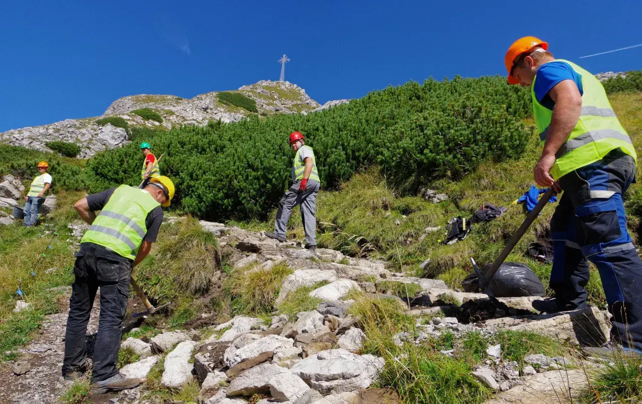 Pracownicy konserwują szlak na Giewont. Czy szlak na Giewont jest trudny? Widać krzyż na szczycie, a teren jest kamienisty.