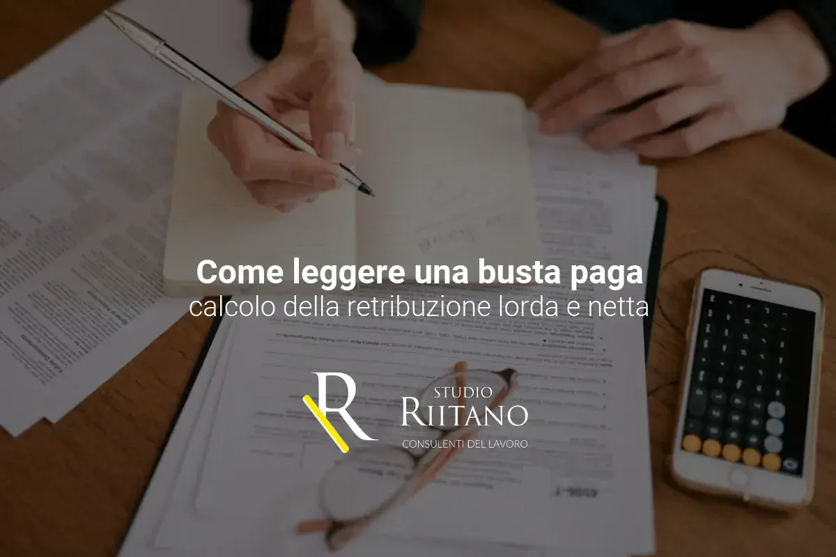 Mani che scrivono su un quaderno, fogli, smartphone con calcolatrice e occhiali. Il testo parla di come leggere la busta paga, calcolando contributi previdenziali e retribuzione.