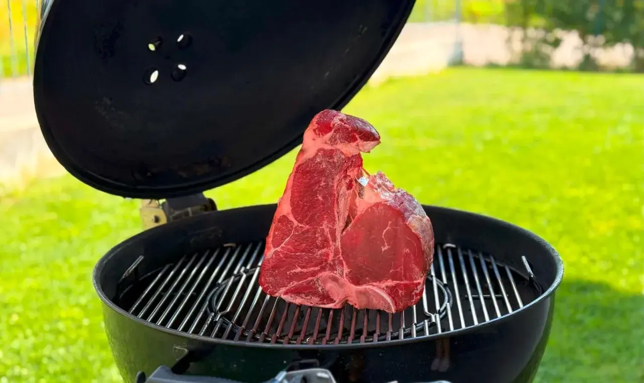 Una succulenta bistecca alla fiorentina cruda riposa sulla griglia di un barbecue, pronta per essere cucinata all'aperto.
